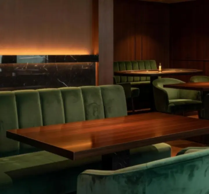 Sfeervol interieur van Lumiar Room met diepe groene tinten, donkere houten tafels en warme amberverlichting.